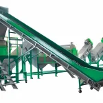Das Bild zeigt eine Waschanlage für Hartkunststoffe in einer industriellen Umgebung, die überwiegend in leuchtendem Grün gehalten ist. Das umfassende System besteht aus einer Reihe mechanischer Komponenten: einem großen Trichter, einem Schrägförderband für den Materialtransport und mehreren Sortier- und Waschstationen. Jede Station ist mit Sicherheitsgeländern ausgestattet und steht auf stabilen grünen Rahmen, die die robuste Konstruktion und die Sicherheitsmaßnahmen unterstreichen. Die Anlage ist für die effiziente Verarbeitung großer Mengen von Hartkunststoffen ausgelegt und gewährleistet eine gründliche Reinigung und Vorbereitung für weitere Recyclingschritte. Diese stromlinienförmige Einrichtung unterstreicht die industrielle Technologie, die sich der nachhaltigen Bewirtschaftung von Kunststoffabfällen widmet.