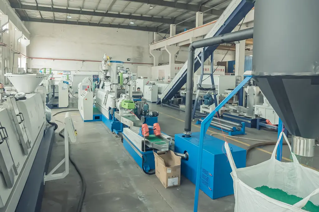 The picture presents a comprehensive industrial setup dedicated to plastic recycling and processing. It showcases a series of interconnected machines and equipment, forming a complete production line to handle, treat, and transform plastic waste into reusable pellets or granules. Key Observations: Multiple Stages: The facility is organized into distinct stages, each with specialized equipment, suggesting a multi-step recycling and processing approach. Conveyor Systems: A network of conveyor belts, both horizontal and inclined, transports plastic materials between different processing stages. Variety of Machines: The line includes diverse machines, indicating various treatment processes such as shredding, washing, drying, extruding, and pelletizing. Extrusion Line: The central component is an extrusion line, consisting of an extruder and a pelletizer. The extruder melts and homogenizes the plastic material, while the pelletizer cuts the extruded plastic into uniform pellets. Feeding and Storage: Hoppers, silos, and large bags are present for feeding materials into the system and storing processed plastic pellets. Control Systems: Control panels and automation equipment are visible, indicating precise control and monitoring of the process parameters. Potential Processing Steps: Pre-processing (Not Fully Visible): This stage may involve sorting, shredding, and washing the plastic waste to remove contaminants and prepare it for further processing. Extrusion: The cleaned plastic flakes or granules are fed into the extruder, where they are melted and homogenized under controlled temperature and pressure. Filtration (Possible): A filtration system might be present to remove any remaining impurities from the molten plastic. Pelletizing: The molten plastic is then extruded through a die and cut into uniform pellets by the pelletizer. Cooling and Drying: The pellets are cooled and dried to ensure their stability and quality. Storage and Packaging: The finished plastic pellets are stored in silos, bags, or other containers for transportation or further processing. Applications and Benefits: Circular Economy: The facility contributes to a circular economy by converting plastic waste into reusable material, reducing reliance on virgin plastics and minimizing environmental impact. Resource Recovery: It recovers valuable resources from discarded plastics, preventing them from ending up in landfills or polluting the environment. Sustainable Manufacturing: The recycled plastic pellets can be used to manufacture various new products, promoting sustainable practices in multiple industries. Economic Advantages: Plastic recycling can offer economic benefits by reducing waste disposal costs and creating value from discarded materials. Overall, the picture portrays a sophisticated and efficient plastic recycling and processing facility that plays a significant role in promoting sustainability, resource conservation, and responsible waste management.