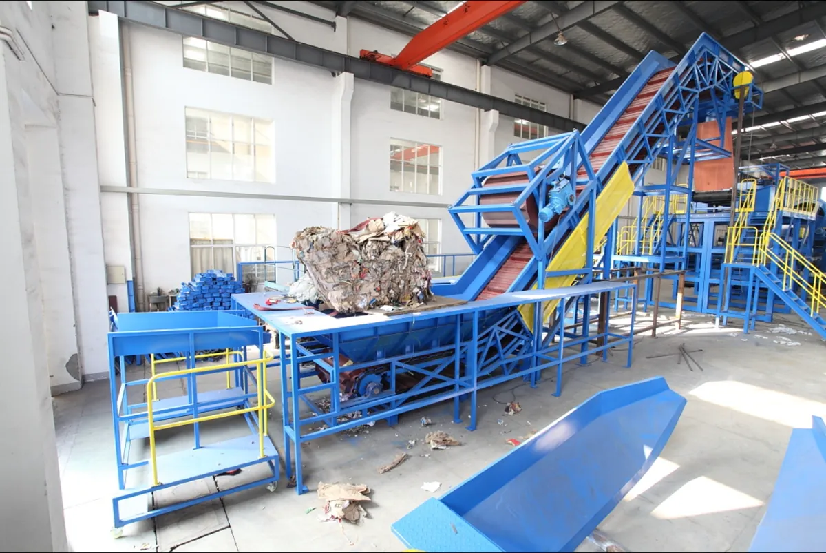 The picture showcases an industrial setting specifically designed for handling and processing recyclable materials, most likely paper and cardboard. The prominent features indicate a focus on sorting, conveying, and potentially baling these materials for further recycling or processing. Key Observations: Conveyor Belt System: The central element is a large, inclined conveyor belt system. It transports the loose paper and cardboard materials upwards, likely towards further sorting or processing stations. Feeding Platform: At the base of the conveyor system, there's a platform where loose materials are loaded. A pile of paper and cardboard is visible, indicating the input source. Sorting Stations (Potentially Out of Frame): While not fully visible, the conveyor system suggests the presence of sorting stations further along the line. These stations could involve manual or automated sorting processes to separate different types of paper or cardboard or remove contaminants. Baling Equipment (Not Visible): The overall setup suggests the possibility of baling equipment located downstream of the sorting stations. Baling compresses the sorted paper and cardboard into compact bales, facilitating efficient storage and transportation for further processing. Industrial Environment: The high ceilings, spacious layout, and presence of an overhead crane indicate an industrial facility designed for handling large volumes of materials. Potential Applications and Processes: Paper and Cardboard Recycling: The facility appears geared towards processing and recycling paper and cardboard waste from various sources, such as households, businesses, or industrial operations. Material Recovery Facilities (MRFs): It could be part of a larger material recovery facility, where different types of recyclable materials are sorted and processed. Paper Mills: The sorted and baled paper and cardboard might be sent to paper mills for repulping and manufacturing new paper products. Benefits: Waste Reduction and Resource Recovery: The facility plays a vital role in diverting paper and cardboard waste from landfills, promoting recycling and resource recovery. Environmental Sustainability: Recycling paper and cardboard reduces the demand for virgin materials, conserves natural resources, and lowers greenhouse gas emissions associated with paper production. Economic Benefits: The recycled paper and cardboard can be used to manufacture new products, supporting a circular economy and creating jobs within the recycling and manufacturing sectors. Overall, the picture depicts an essential stage in the paper and cardboard recycling process, contributing to environmental sustainability and resource conservation efforts.