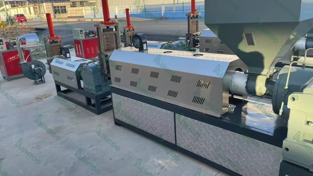 The image shows a lineup of various industrial machines, likely used for material processing such as crushing or grinding. The machines are equipped with motors, protective housings, and hoppers for feeding material. The design suggests these are part of a larger processing facility, possibly for recycling or manufacturing operations. The machinery is installed outdoors, indicating a robust design suitable for heavy-duty operations. The presence of multiple units in different sizes and with different configurations suggests a versatile processing line capable of handling various materials or tasks.