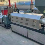 The image shows a lineup of various industrial machines, likely used for material processing such as crushing or grinding. The machines are equipped with motors, protective housings, and hoppers for feeding material. The design suggests these are part of a larger processing facility, possibly for recycling or manufacturing operations. The machinery is installed outdoors, indicating a robust design suitable for heavy-duty operations. The presence of multiple units in different sizes and with different configurations suggests a versatile processing line capable of handling various materials or tasks.