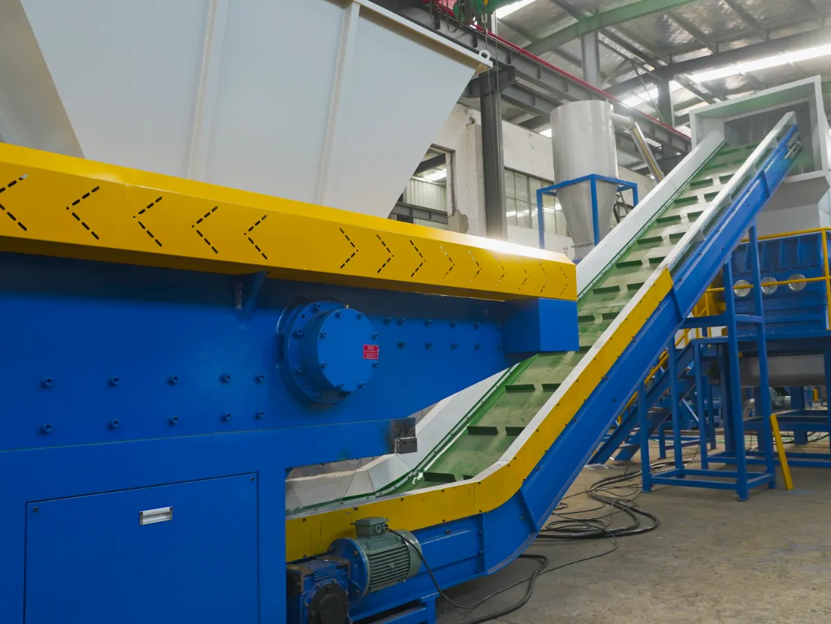 depicts a segment of industrial recycling equipment, possibly within a plastic recycling facility. The prominent blue machine with a yellow conveyor belt suggests it is part of a material handling system designed to transport plastic waste to different stages of the recycling process, such as sorting, washing, or shredding. The construction of the machinery indicates heavy-duty use, likely capable of handling large volumes of materials. The blue and yellow colors are not only aesthetic but also function as visual cues for safety and operational purposes. The staircase and platform structure in the background provide access to higher parts of the machinery for maintenance or to manage the recycling process. The presence of various hoppers and conduits suggests a sophisticated system to manage and direct the flow of materials through the recycling process. The investment in such machinery typically reflects a commitment to efficient, high-volume processing of recyclable materials to turn waste into reusable raw materials.