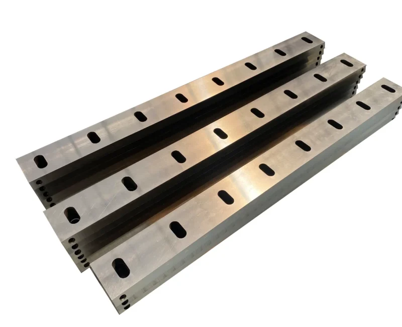 industrial cutting blades, typically used in plastic crushers or granulators. These blades are manufactured to fit into machinery that shreds plastic into smaller pieces for recycling purposes. The holes along the blades are for mounting them securely within the machine, and the slots are likely designed to reduce the weight of the blades, to enhance cutting efficiency, or to serve a specific purpose related to the material they are intended to cut. The material appears to be high-quality steel, which is necessary for durability and maintaining a sharp edge during the intensive process of cutting through plastic materials. The precise manufacturing and finishing suggest that these blades are made for heavy use in an industrial environment where they would be subjected to considerable wear and tear.