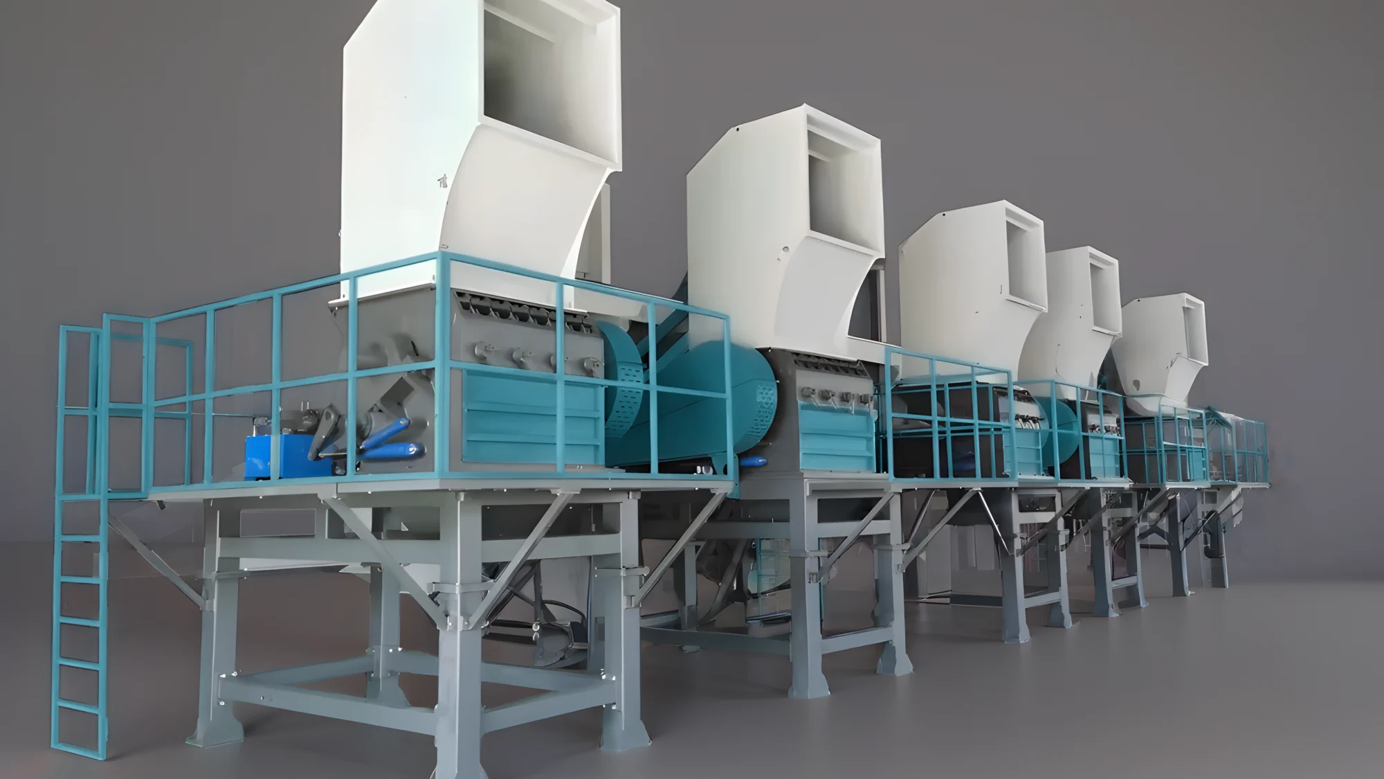 The image shows machinery that is consistent with a plastic crushing or recycling system. In a typical setup, plastic crushers are used to reduce plastic waste into smaller, more manageable pieces or granules. These machines can be part of a larger recycling line that includes several stages, such as sorting, washing, crushing, drying, and pelletizing. The machines in the image have a modular design, with each unit equipped with its own feeding hopper and crushing mechanism. The blue structures likely provide support and possibly contain conveyance systems to move crushed materials to the next stage of processing. The design suggests a heavy-duty operation, capable of handling large volumes of material. These systems are crucial in recycling operations to manage and repurpose plastic waste, thereby contributing to sustainability and environmental conservation efforts.