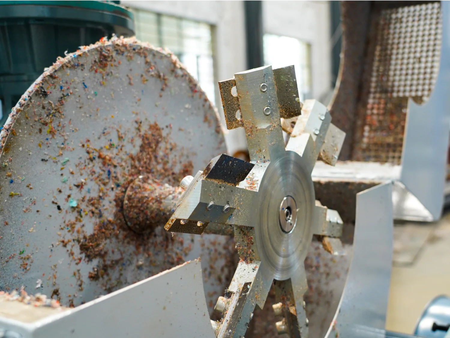 Das Bild scheint einen Teil einer Maschine zur Materialverarbeitung zu zeigen. Es zeigt insbesondere einen metallischen Rotor oder eine Schneidklinge, die mit verarbeitetem Material bedeckt ist, was möglicherweise darauf hindeutet, dass es sich um einen Teil eines Kunststoffgranulators oder einer Zerkleinerungsmaschine handelt. Diese Maschine wird typischerweise in Recycling- oder Fertigungsanlagen verwendet, um Kunststoff oder andere Materialien in kleinere Granulate zu zerlegen, die dann wiederverwendet oder weiterverarbeitet werden können. Das abgenutzte und abwechslungsreiche Aussehen des Materials auf dem Rotor lässt auf eine Ansammlung verschiedener zerkleinerter Substanzen schließen.