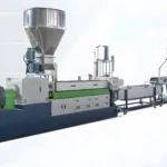 The image shows an industrial plastic extrusion line. This machinery is used for the production of plastic products by melting raw plastic material and forming it into a continuous profile. The equipment includes various components such as a hopper for raw material input, an extruder where the plastic is melted and pushed through a die to shape it, cooling systems, and possibly cutting or rolling mechanisms for the final product handling. The setup is typically used in manufacturing processes for creating plastic pipes, sheets, films, and other profiles.