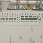 The picture shows an industrial control panel or system console. It has a large array of buttons, indicator lights, digital displays, knobs, and switches that appear to be used for operating and monitoring some kind of machinery or manufacturing process. The control panel has various colored buttons (red, blue, orange, yellow) likely representing different functions or commands. There are numeric digital readouts displaying values like temperatures or measurements. The overall setup suggests this is the user interface for controlling complex industrial equipment or an automated production line.