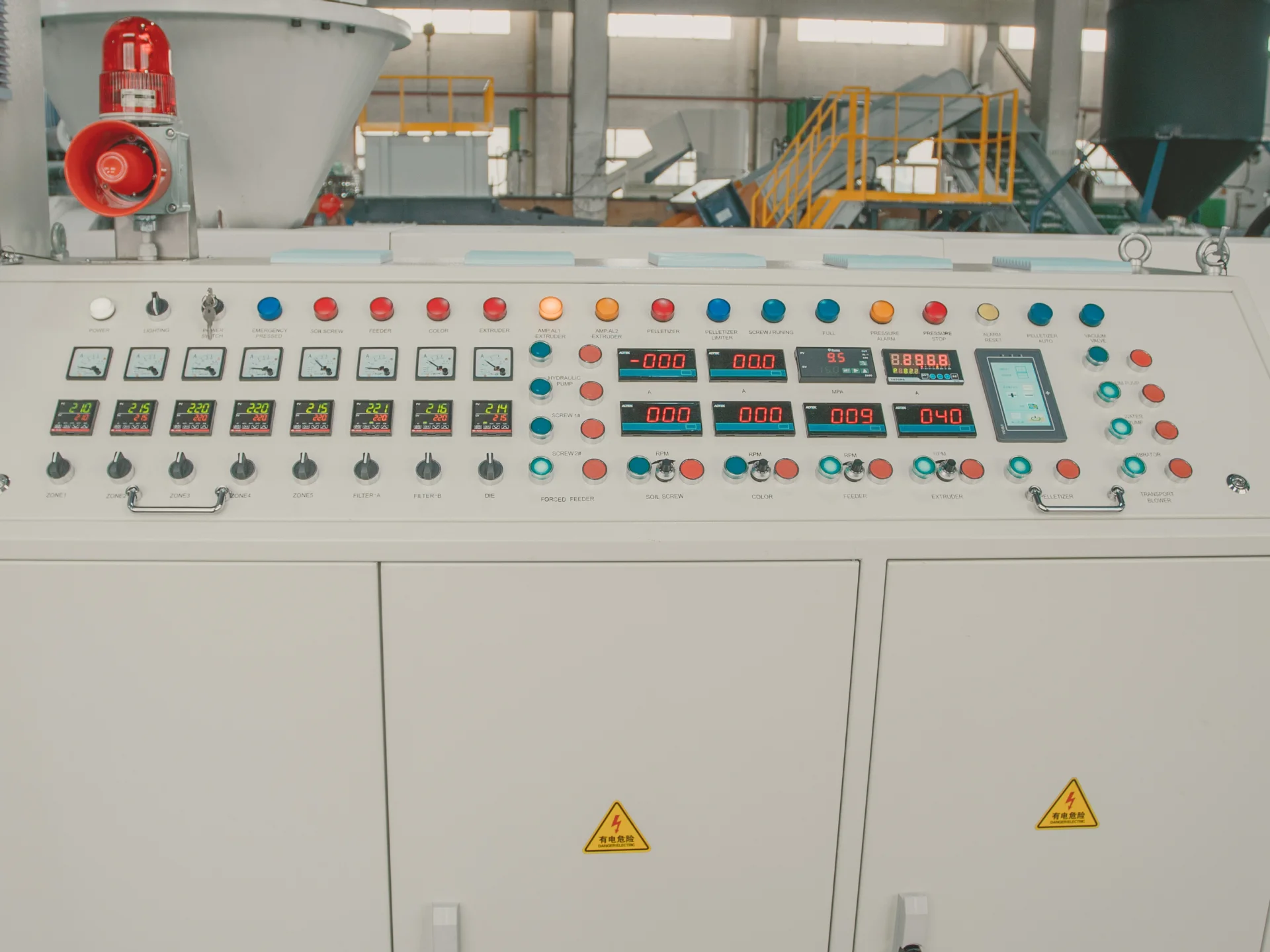 The picture shows an industrial control panel or system console. It has a large array of buttons, indicator lights, digital displays, knobs, and switches that appear to be used for operating and monitoring some kind of machinery or manufacturing process. The control panel has various colored buttons (red, blue, orange, yellow) likely representing different functions or commands. There are numeric digital readouts displaying values like temperatures or measurements. The overall setup suggests this is the user interface for controlling complex industrial equipment or an automated production line.