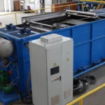 Dissolved Air Flotation (DAF) system in a plastic recycling facility, featuring a large blue tank with metal components and an adjacent control panel.